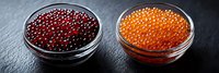 Red and orange caviar in glass bowls on dark stone background, fresh luxury seafood appetizer served as gourmet delicacy. Panoramic food composition.