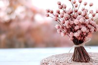 Delicate pink cotton stems arranged in rustic bouquet with twine on textured surface against soft blurred background, creating romantic farmhouse atmosphere.