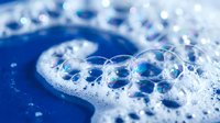 Soap bubbles floating on blue water surface with foam creating abstract cleaning and hygiene concept for household products and bathroom accessories.