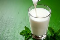Fresh milk pouring into clear glass with mint leaves on green wooden background, dairy drink splash captured in motion, natural organic beverage.