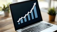 Laptop screen displaying ascending bar graph with upward arrow trend in blue and white on dark background, with blurred office plants in background.
