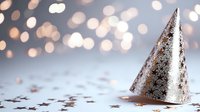 Silver party cone hat with glitter stars pattern on blurred bokeh background with scattered metallic confetti, festive celebration mood and soft lighting.