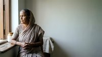 Senior woman wearing traditional headscarf sitting by window in contemplative pose, suitable for editorial, lifestyle, and cultural storytelling projects.