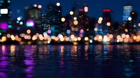 Blurred city lights reflecting on water surface at night with vibrant bokeh effect creating magical urban landscape with purple and golden glows.