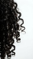 Close-up of dark black curly hair with tight spiral ringlets on a light background, showcasing natural texture for haircare and beauty concepts.