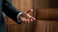 Professional businessman extending open hand for handshake in modern office interior with leather furniture background for business partnership concepts.
