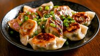 Asian dumplings with crispy bottom, garnished with green onions on black ceramic plate. Steamed and pan-fried potstickers served on wooden table.