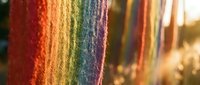 Vibrant rainbow colored textile threads arranged in spectrum order creating colorful fabric background for craft and sewing projects.
