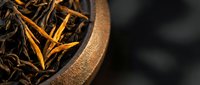 Dried tea leaves and orange peel in wooden bowl on dark background, suitable for beverage packaging, wellness blogs, and tea product marketing.