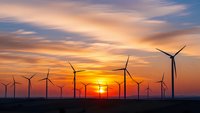 Wind turbines silhouetted against dramatic sunset sky with orange and purple clouds, renewable energy farm generating clean electricity at golden hour.