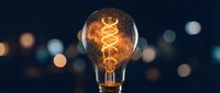 Vintage incandescent bulb with glowing filament against blurred bokeh background, representing innovation, energy, creativity, and ideas for design and marketing projects.