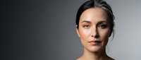 Young woman with natural makeup and pulled back hair against gray gradient background for beauty and skincare campaigns.