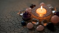 Healing crystals and gemstones arranged around glowing candle on wooden holder creating peaceful meditation and spiritual wellness atmosphere.