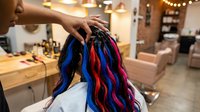Hairstylist showing colorful hair extensions in vibrant blue, red, and purple shades to client in modern salon setting for hair design consultation.
