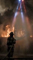 Firefighter silhouette battling intense flames with dramatic smoke and emergency vehicle lights creating atmospheric rescue scene for safety campaigns.