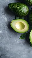 Fresh ripe avocado cut in half showing creamy flesh and pit on dark concrete background with green leaves, dramatic lighting for food photography.