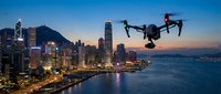 Professional drone flying over illuminated city skyline at dusk with harbor lights reflecting on water for aerial photography and urban exploration.