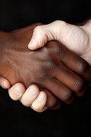 Close-up of interracial handshake against black background showing unity, partnership and cooperation between people of different races and cultures.