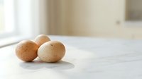 Fresh brown chicken eggs on white marble counter in bright modern kitchen with natural sunlight streaming through window for cooking and baking recipes.