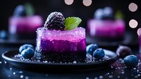 Purple berry mousse dessert with dark cookie base garnished with fresh blackberry and mint leaf on black plate, surrounded by blueberries and bokeh lights.