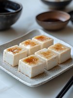 Creamy tofu dessert squares with caramelized sugar topping served on ceramic plate, traditional Asian fusion cuisine style with modern presentation.