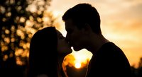Romantic couple silhouette kissing at golden sunset with warm bokeh lights creating intimate atmosphere for love and relationship concepts.