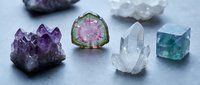 Collection of healing crystals and gemstones including amethyst cluster, watermelon tourmaline slice, clear quartz points and fluorite cube for meditation.