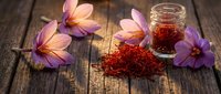 Saffron spice threads with purple crocus flowers on rustic wooden background. Premium culinary ingredient for gourmet cooking and traditional recipes.