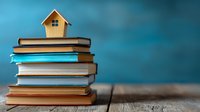 Miniature wooden house on stack of colorful books against blue background, symbolizing home education, property investment, or real estate knowledge.