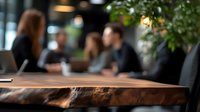 Young diverse business team collaborating at wooden table in modern office space with natural light and green plants, selective focus on foreground surface.