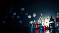 Laboratory glassware with colorful chemical solutions and microscope on dark background with bokeh lights for scientific research and education.