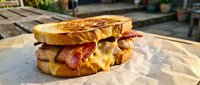 Grilled cheese sandwich with crispy bacon and melted cheese on golden toasted bread served on parchment paper for comfort food and restaurant menu concepts.