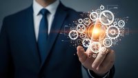 Professional businessman in dark suit holding glowing lightbulb surrounded by interconnected gear mechanisms representing innovation and strategic thinking.