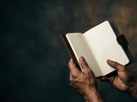 Open notebook with blank lined pages held by hands of a middle-aged man with dark skin tone against dark background, suitable for education, writing, planning, journaling.