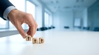 Businessman hand selecting wooden house model in modern office space representing real estate investment and property selection decisions.