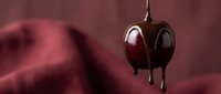 Dark chocolate melting and dripping with rich burgundy fabric background creating luxurious confectionery scene for culinary and dessert marketing materials.