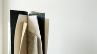 Stack of various paper samples and cardboard sheets in neutral tones arranged vertically, showcasing different textures and materials for crafting projects.