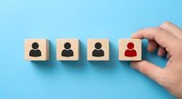 Hand selecting red wooden cube with person icon from row of blocks representing recruitment, hiring, leadership choice, and human resources management.