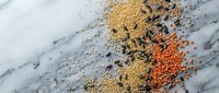 Colorful assorted legumes and grains scattered on marble surface creating organic pattern for healthy cooking and nutrition concepts.