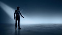 Silhouette of male figure in dark suit standing on reflective surface under dramatic blue light beam from above, conveying concepts of leadership, vision, success, and corporate ambition.