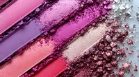 Crushed eyeshadow and lipstick swatches in pink and purple tones with scattered powder makeup texture showing cosmetic product pigmentation.