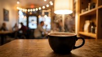 Steaming coffee cup on wooden table in cozy cafe with warm bokeh lights and blurred interior background creating inviting atmosphere for relaxation.
