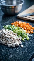Fresh diced vegetables on dark granite countertop with cooking bowl and cutting board in background for meal preparation and healthy cooking recipes.