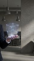 Businessman in dark suit holding glowing digital wireframe cube with connected nodes in modern loft office space for technology and innovation concepts.