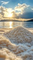 Pile of white sand on beach at sunset with dramatic clouds and mountain silhouette across calm ocean waters.