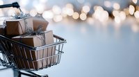 Shopping cart filled with brown kraft paper gift boxes decorated with silver ribbons against blurred bokeh lights background, creating festive holiday atmosphere.