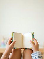 Person holding open blank notebook with colorful spine, wearing striped sleeve and beaded bracelet, for education, reading, writing, and learning concepts.