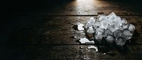 Crushed ice cubes scattered on dark wooden surface with water droplets, suitable for beverage, food and drink, and culinary design projects.