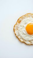 Fresh fried egg with golden yolk on white background, crispy edges and runny center for breakfast cooking and culinary content.