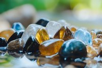 Colorful collection of polished gemstones and crystals including amber, quartz, obsidian and blue stones arranged together for healing and meditation practices.